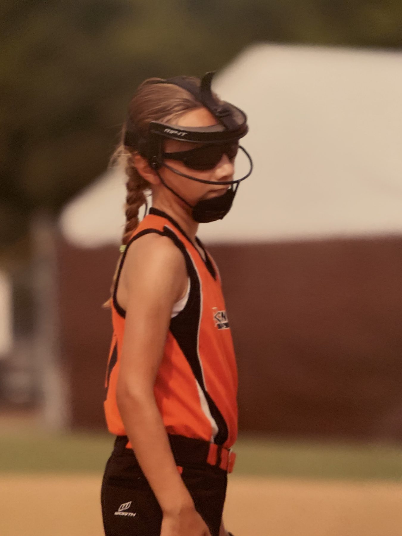 Young Teagan in an orange travel-ball jersey and pitcher's mask