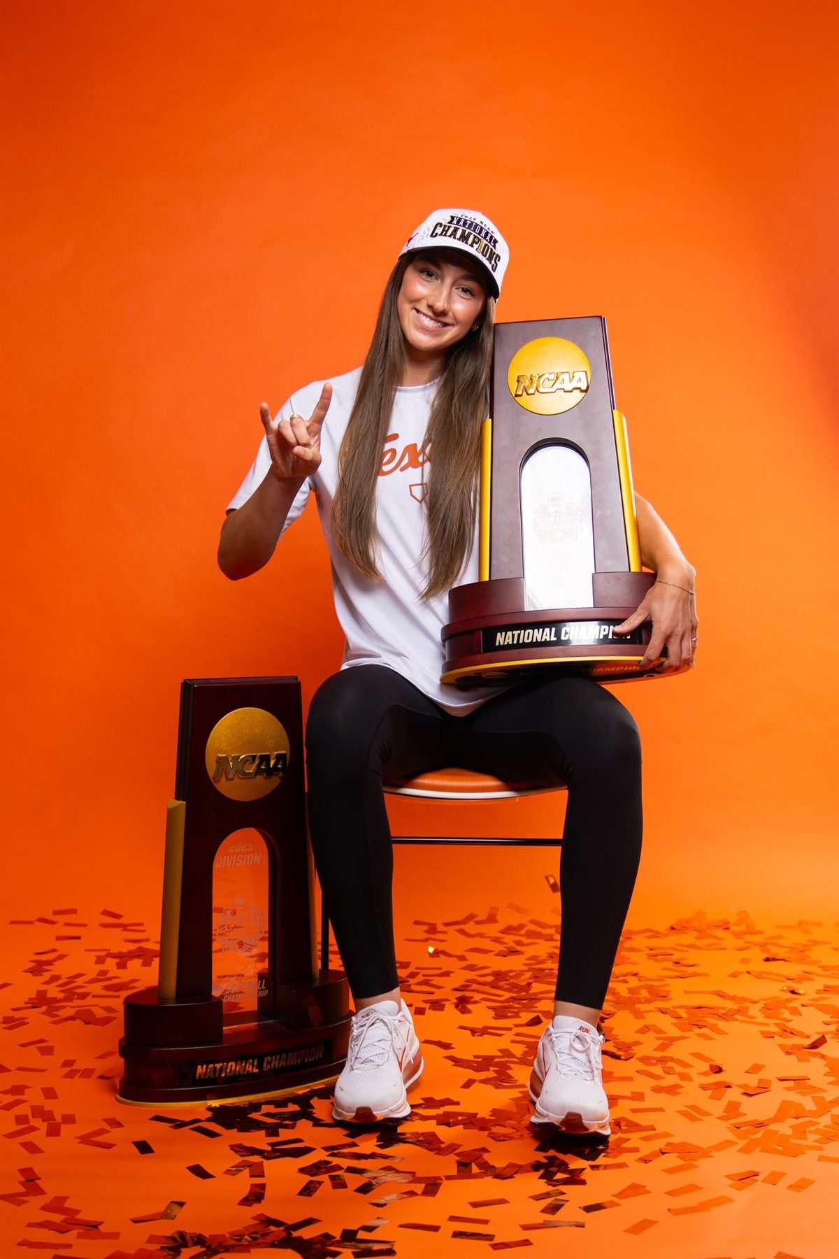 Teagan throwing the Hook 'em sign beside two NCAA national championship trophies